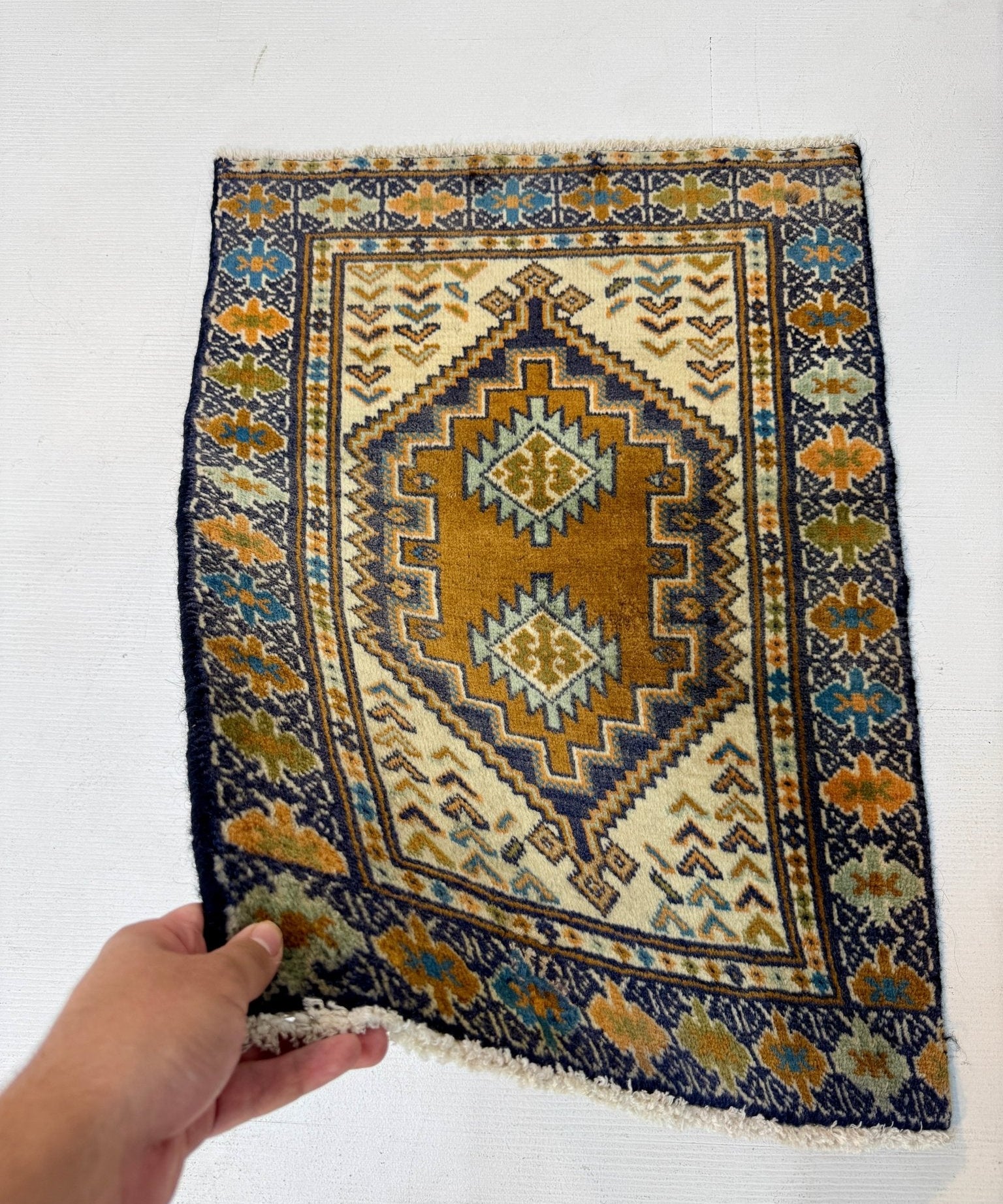 Turkmen rug held by edge; navy frame with tan center diamonds and small orange details