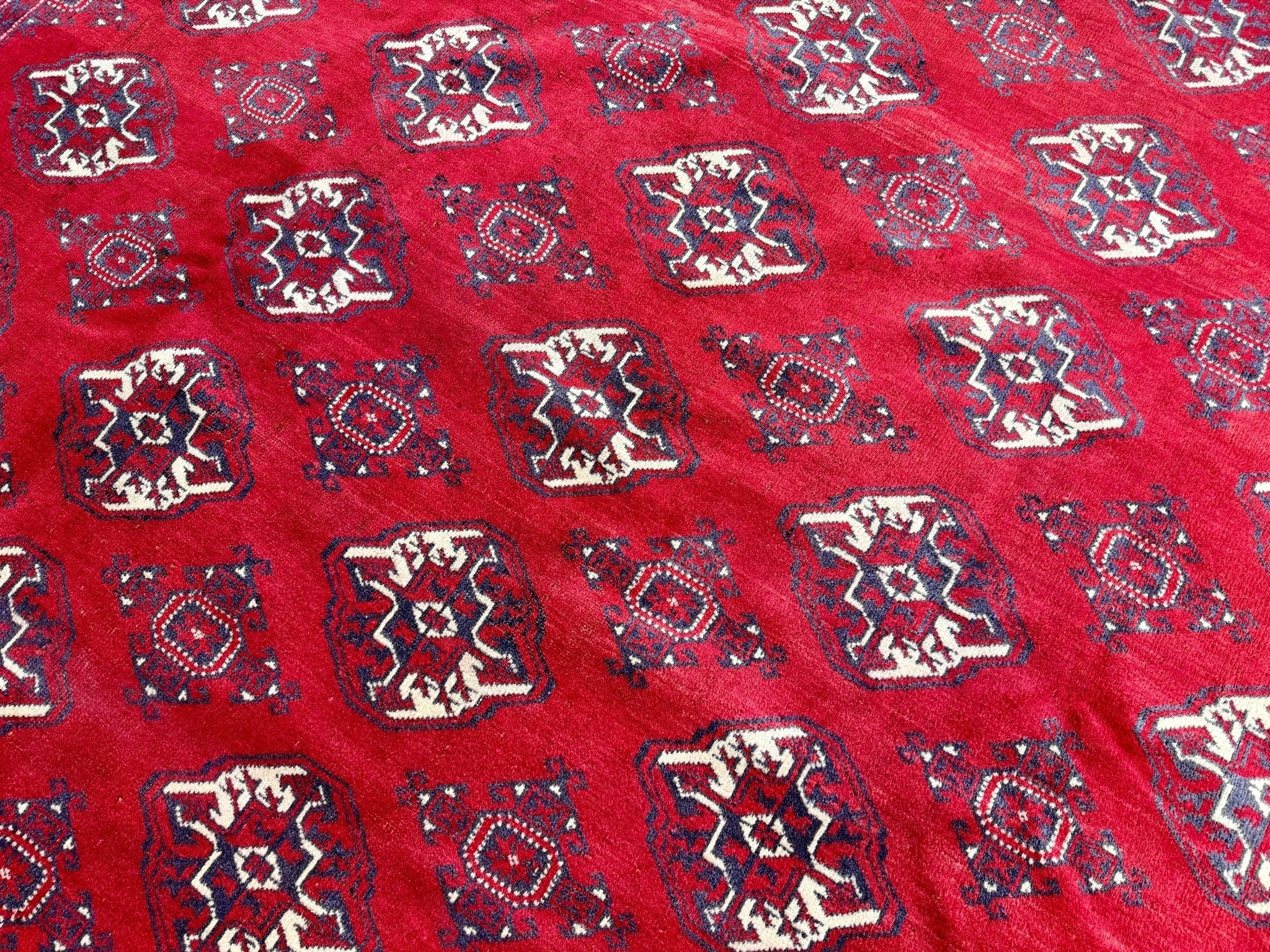 Turkmen rug close-up with red background and rows of small navy-and-white medallions