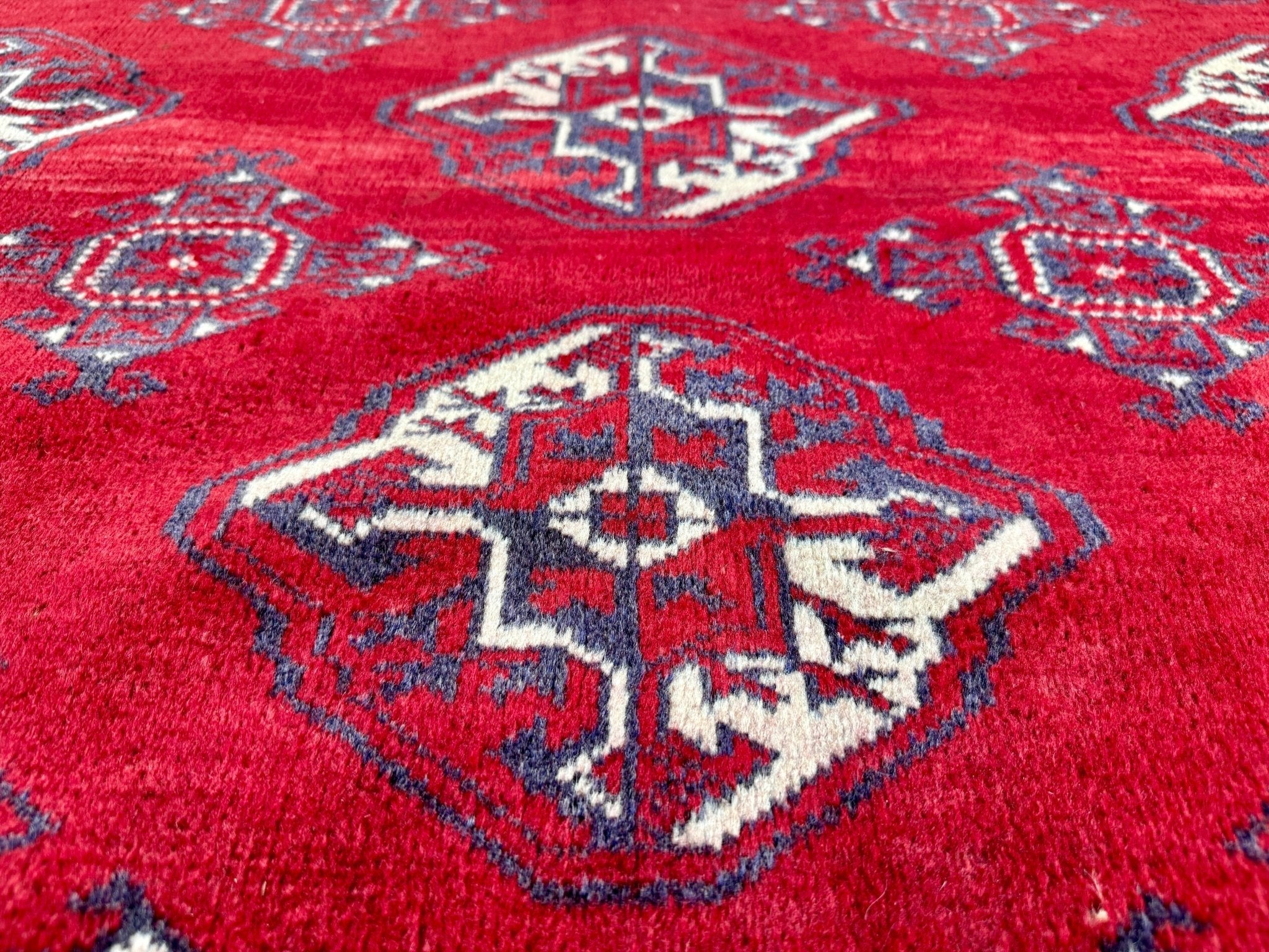 Red rug close-up with navy and cream diamond medallion and symmetrical corner motifs.