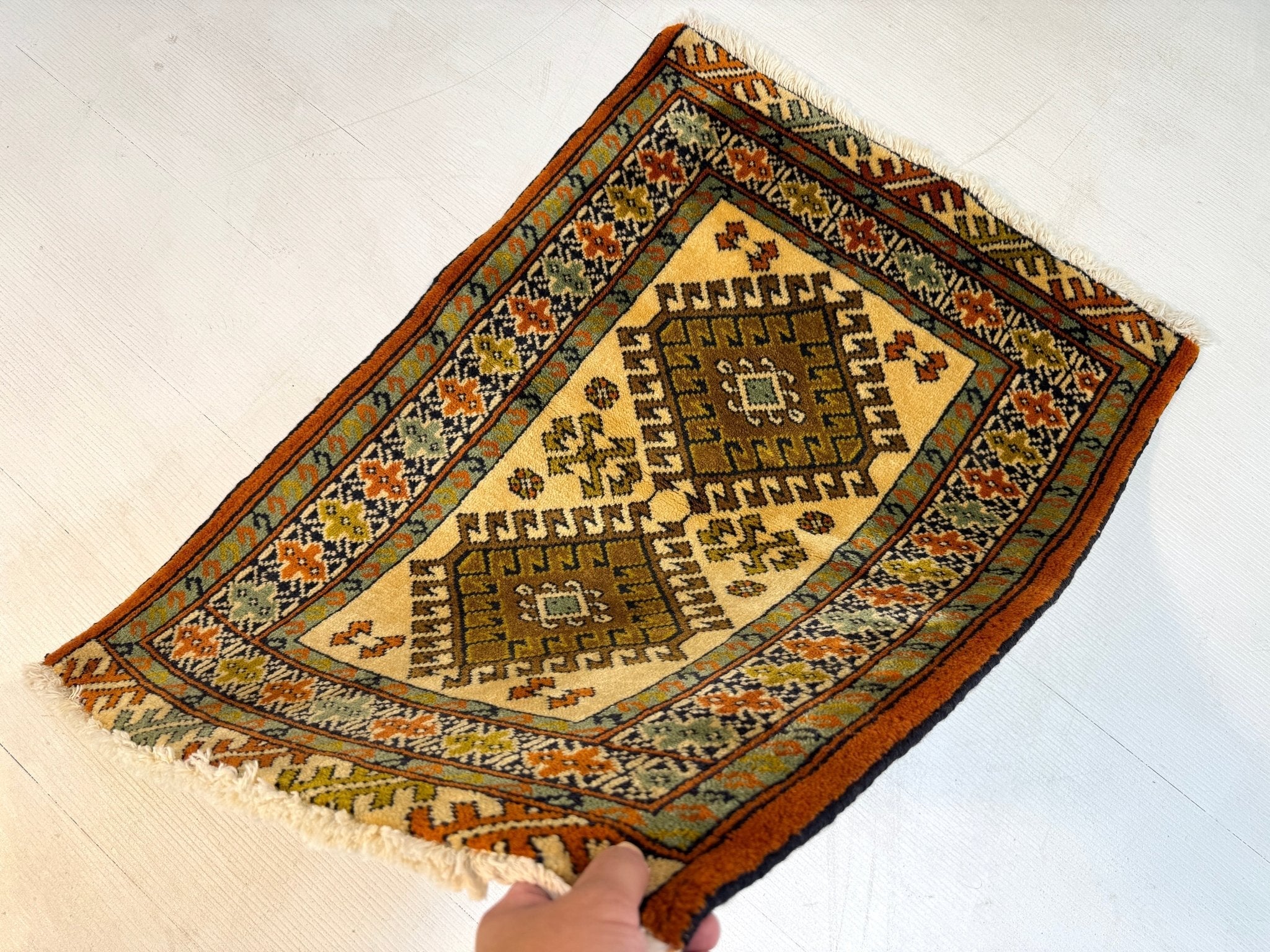 Persian Turkmen rug with diamond medallion, rust border, cream and dark geometric pattern.