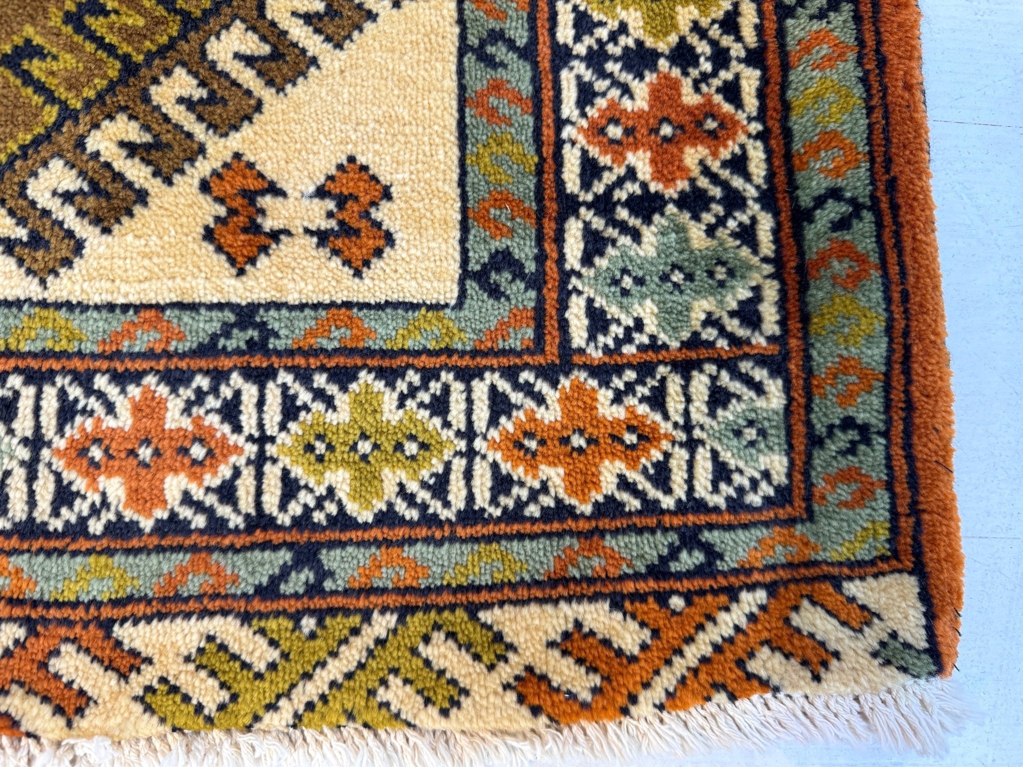 Persian Turkmen rug corner detail with multicolor geometric bands and orange border stripe.