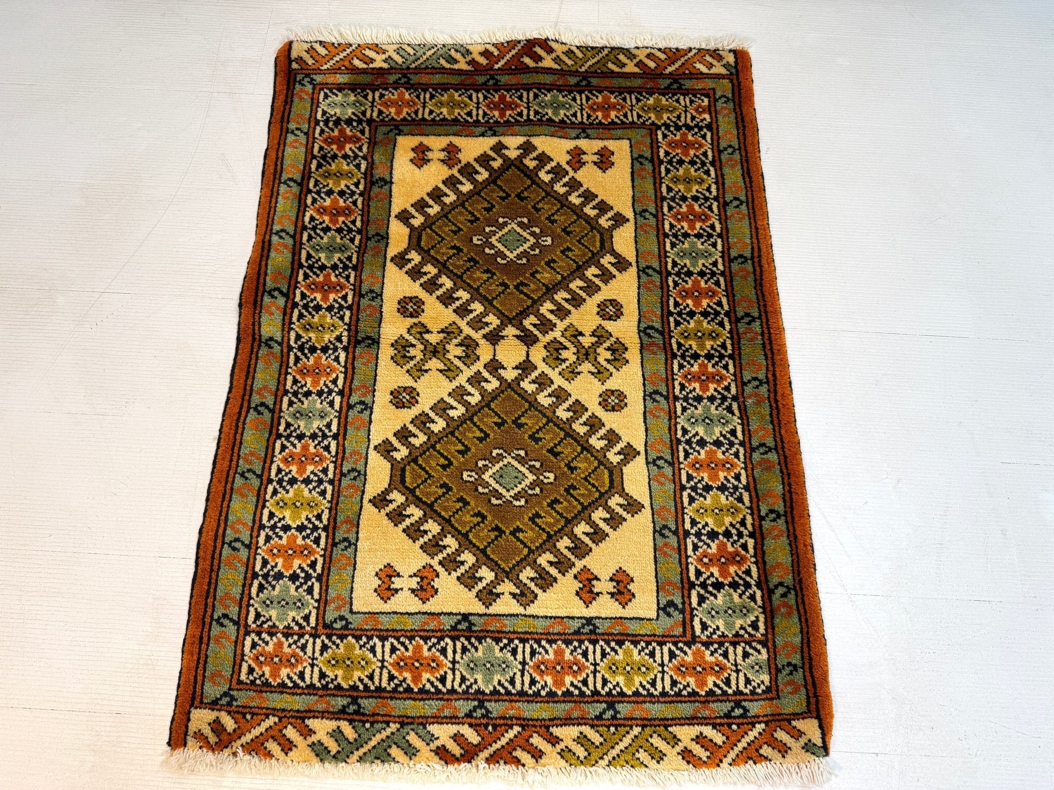 Persian Turkmen rug with central diamond motif, dark border, cream background, geometric details.
