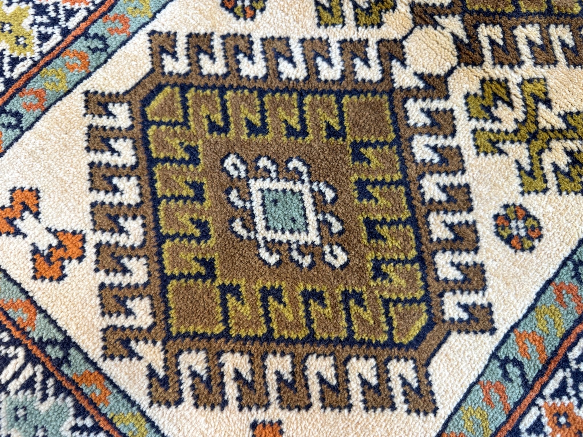 Persian Turkmen rug close-up of central motif, cream field with navy, teal, orange accents.