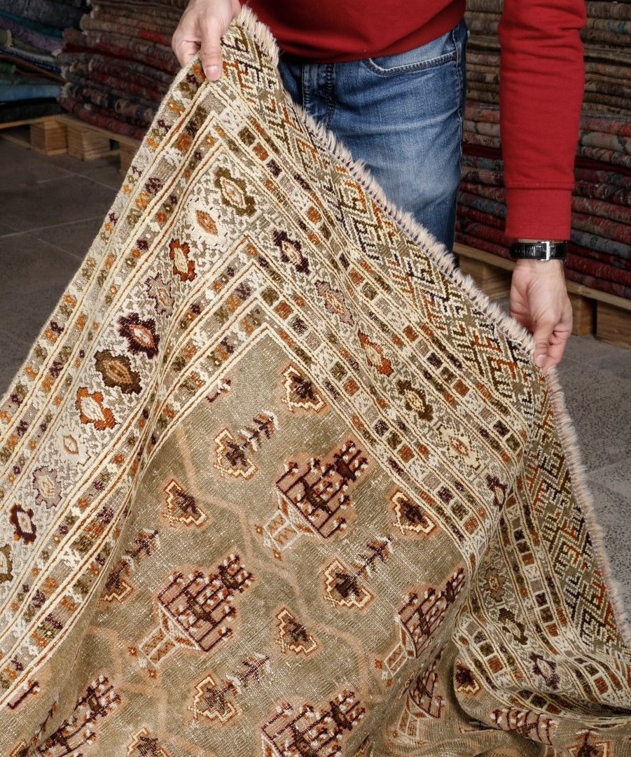 Persian Turkmen rug held up: cream ground with rust and dark motifs, ornate border stripes