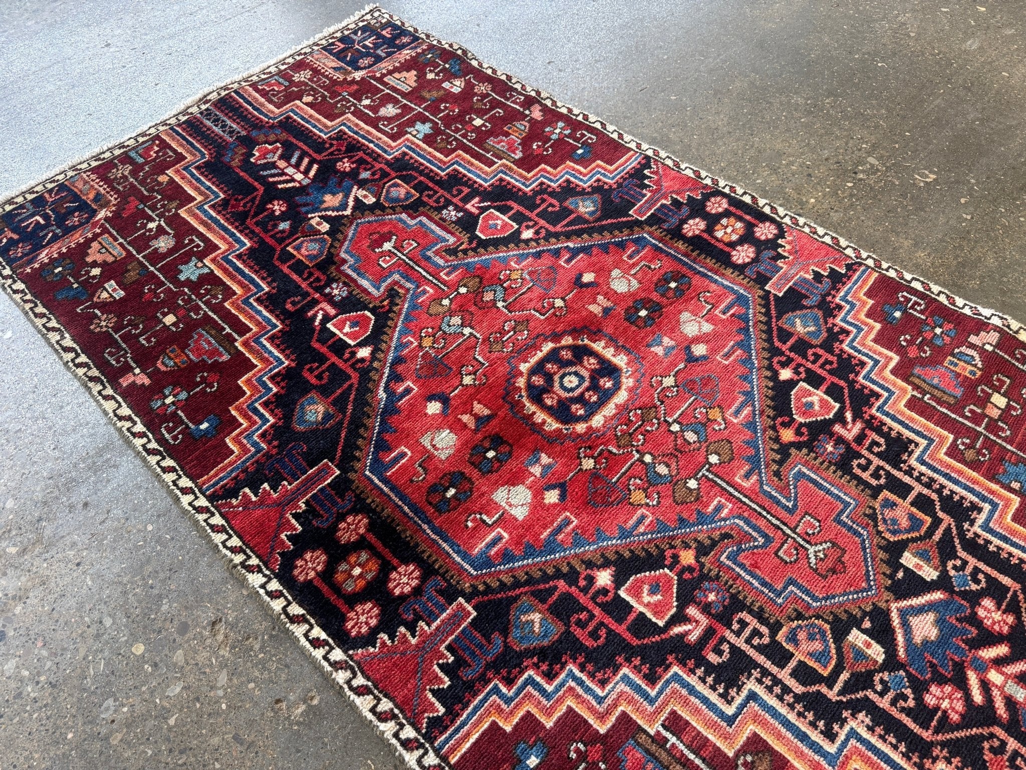 Persian rug close-up with red medallion, navy and cream zigzags, decorative motifs