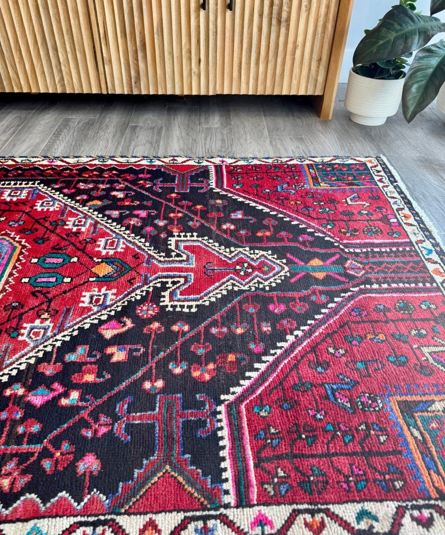 Persian-style red rug with navy and teal ornament panel and cream border lines