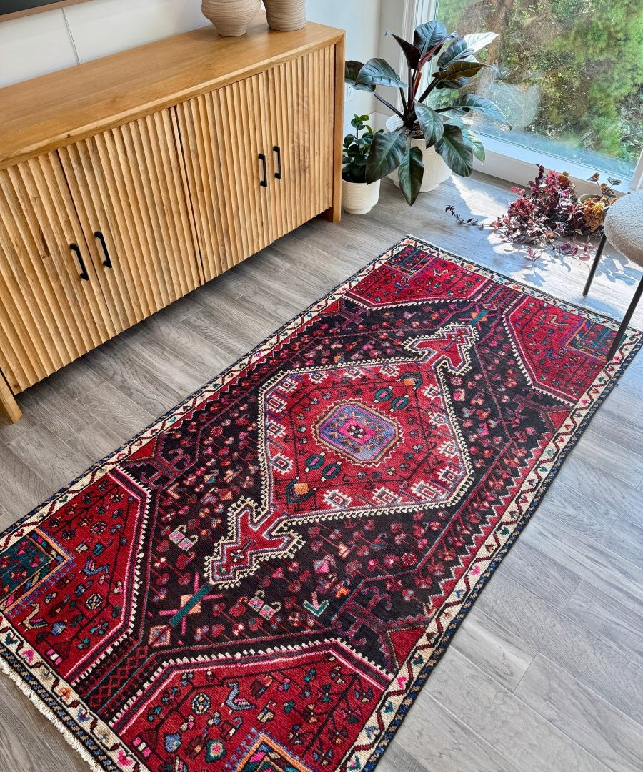 Persian-style red area rug with navy motifs and cream, teal, and pink accents