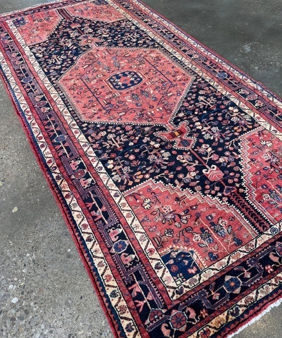 Persian-style area rug, angled view, red and navy fields with ornate medallion and cream edging