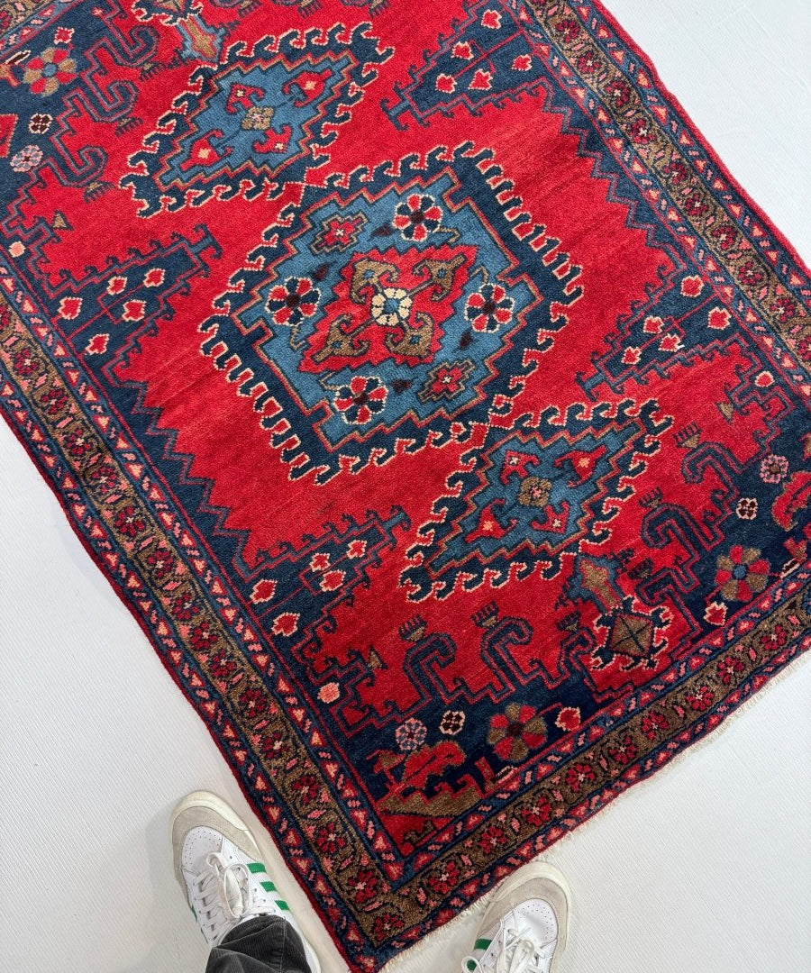 Persian Viss rug angled view with red center medallion and blue geometric border