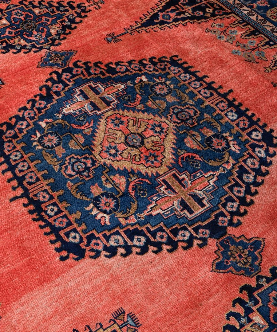 Persian rug close-up, coral-red background with navy starburst medallions