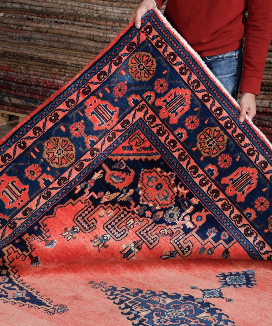 Persian rug corner view, coral-red with navy and orange motif patterns