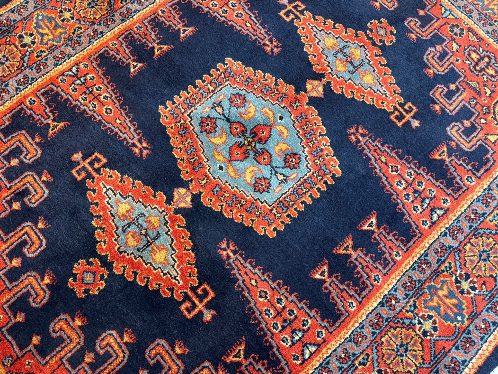 Close-up of navy Persian rug medallion with orange-red, teal, and geometric details