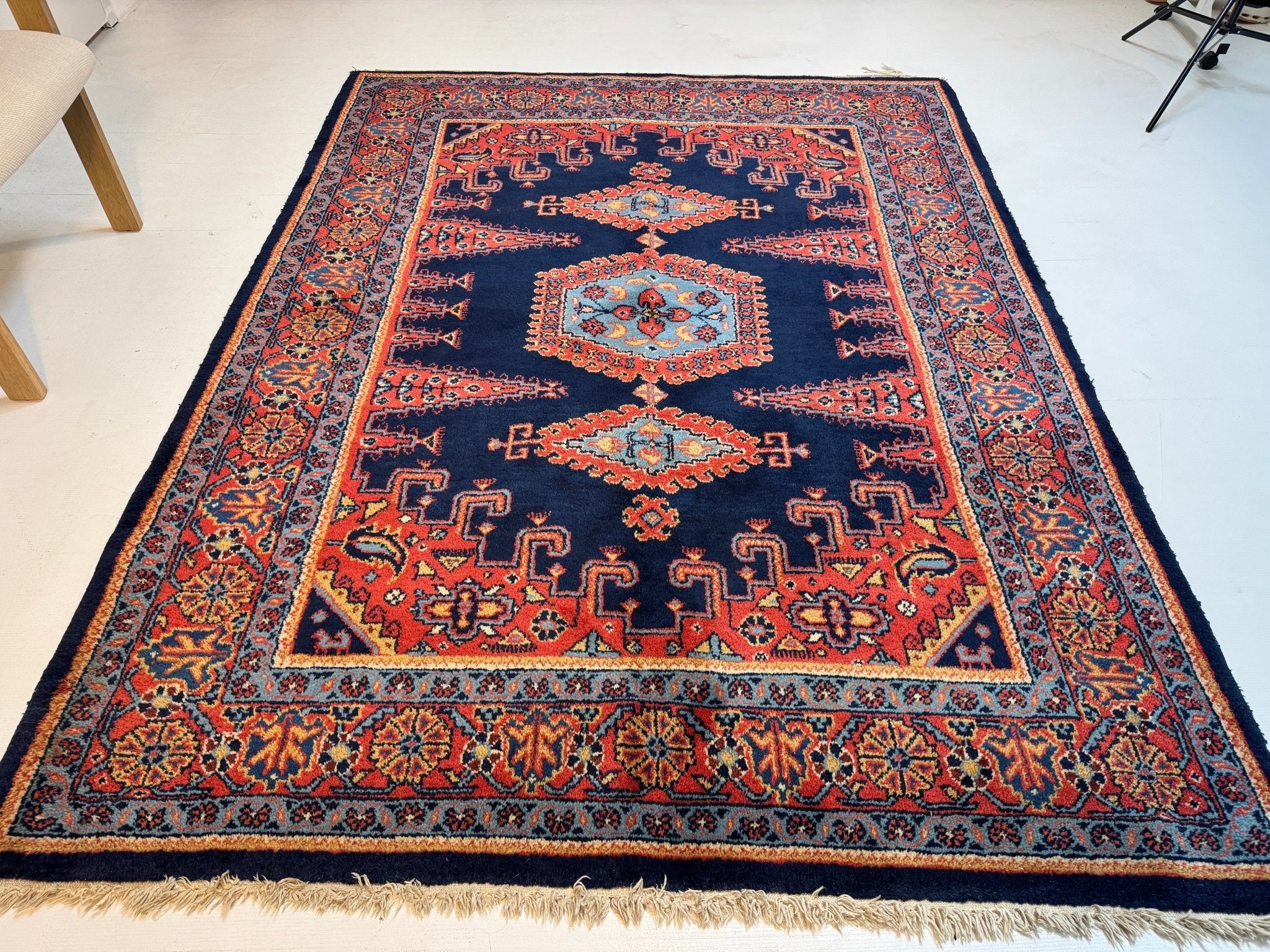 Navy Persian rug with red medallion and decorative border, fringes along the edge