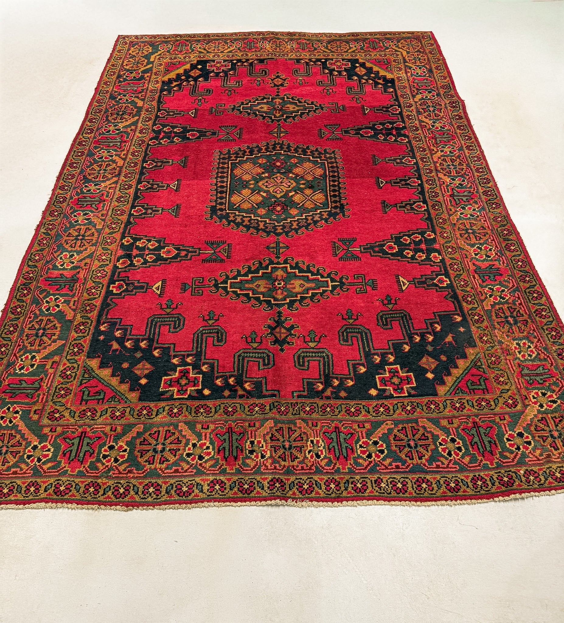Red Persian rug with central medallion, dense geometric motifs, and decorative border