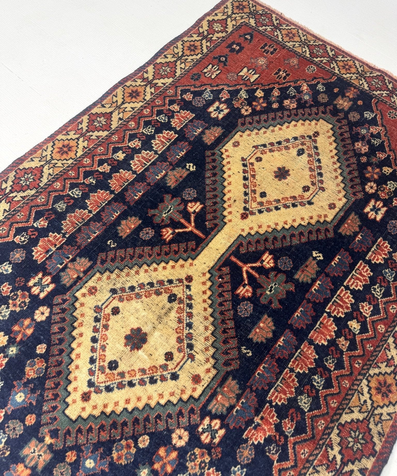 Persian Yalameh rug diagonal view with navy ground, red border, and cream motifs