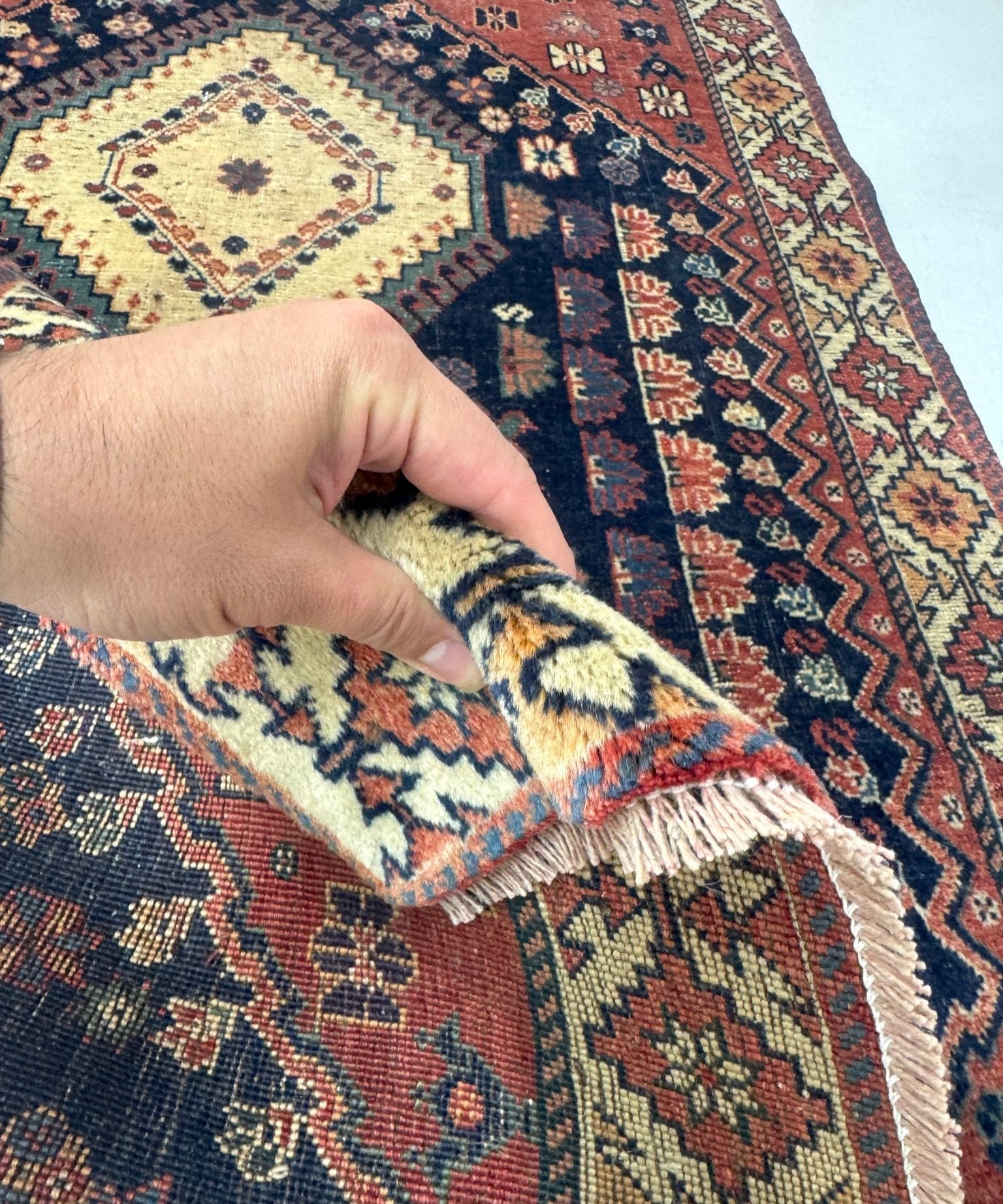 Persian Yalameh rug close-up of fringe edge lifted by hand, navy and cream pattern