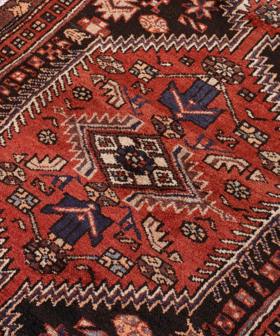 Close-up Persian rug showing dark red field with cream and navy geometric motifs