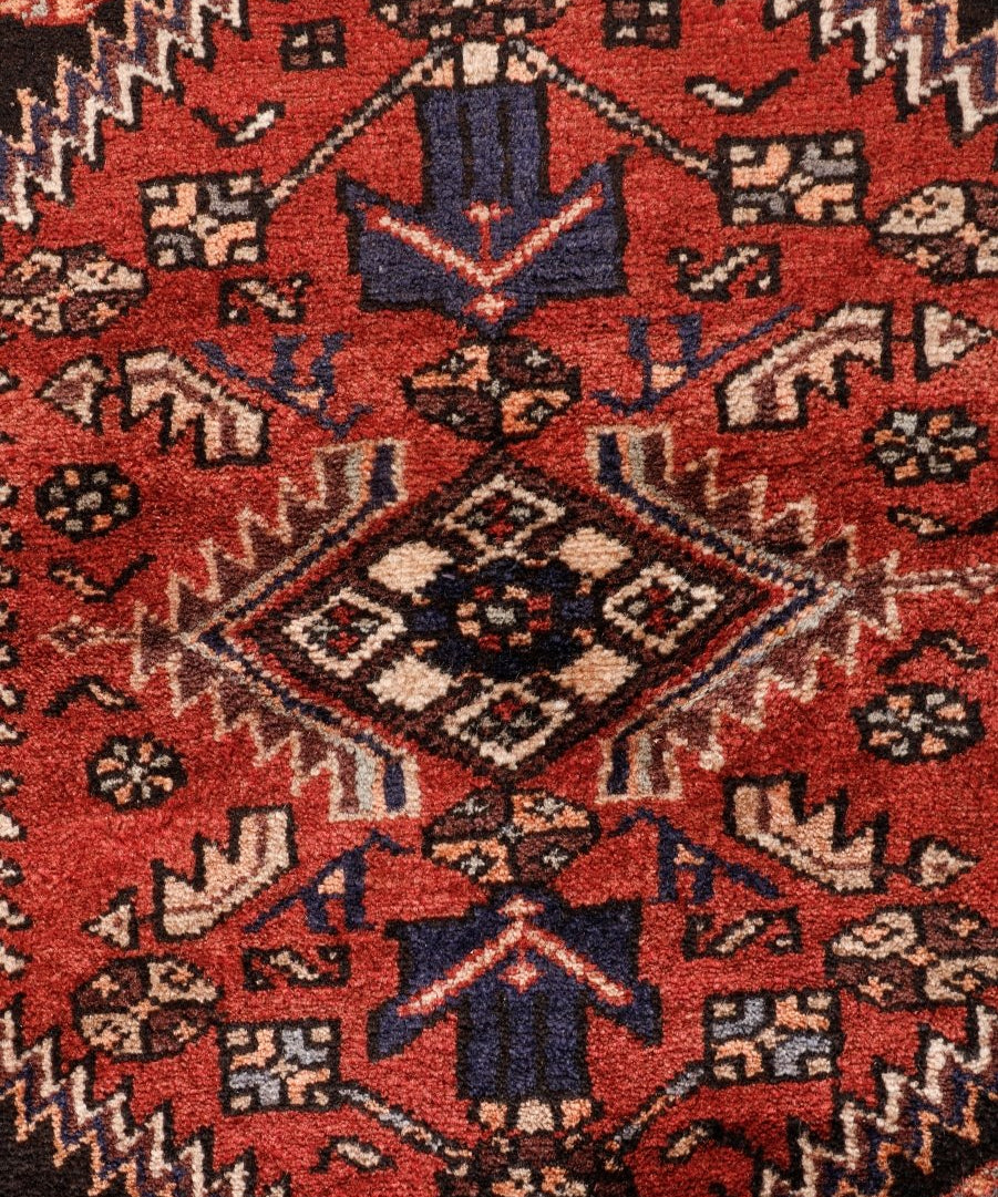 Tight view of Persian rug pattern with dark navy accents, cream diamonds, and red field