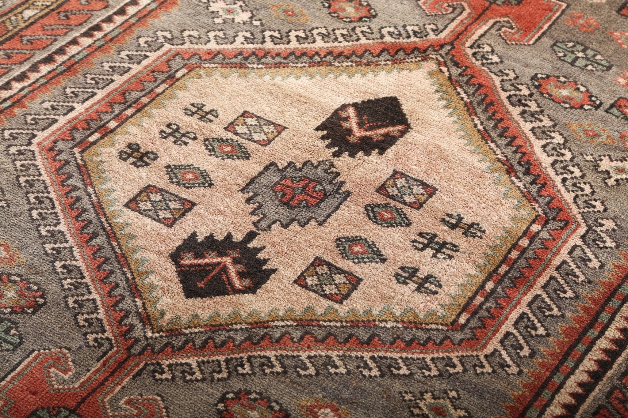 Close-up of rug center panel with small diamond motifs, cream background, rust and gray border.