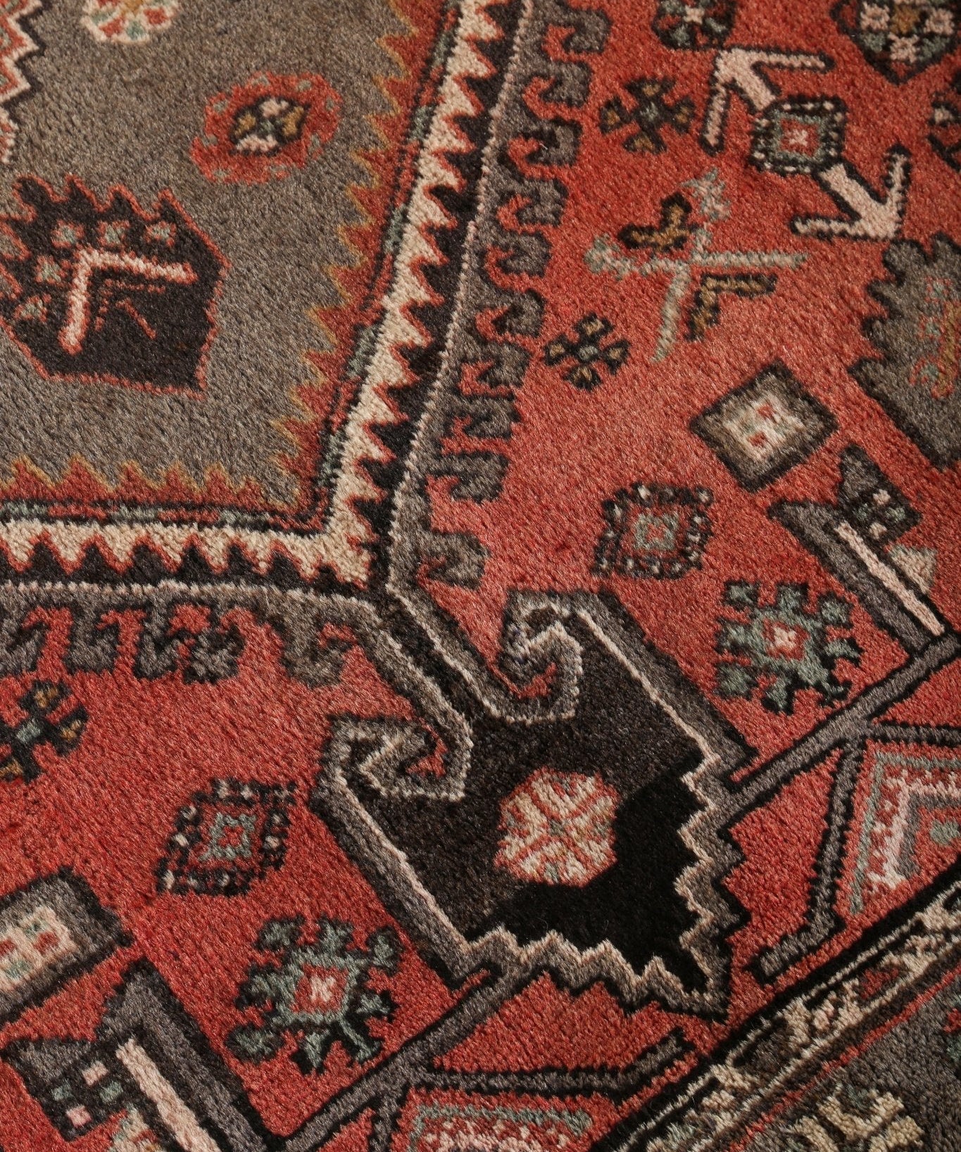 Pattern close-up of rug with rust-red and gray sections, small squares and diamond accents.