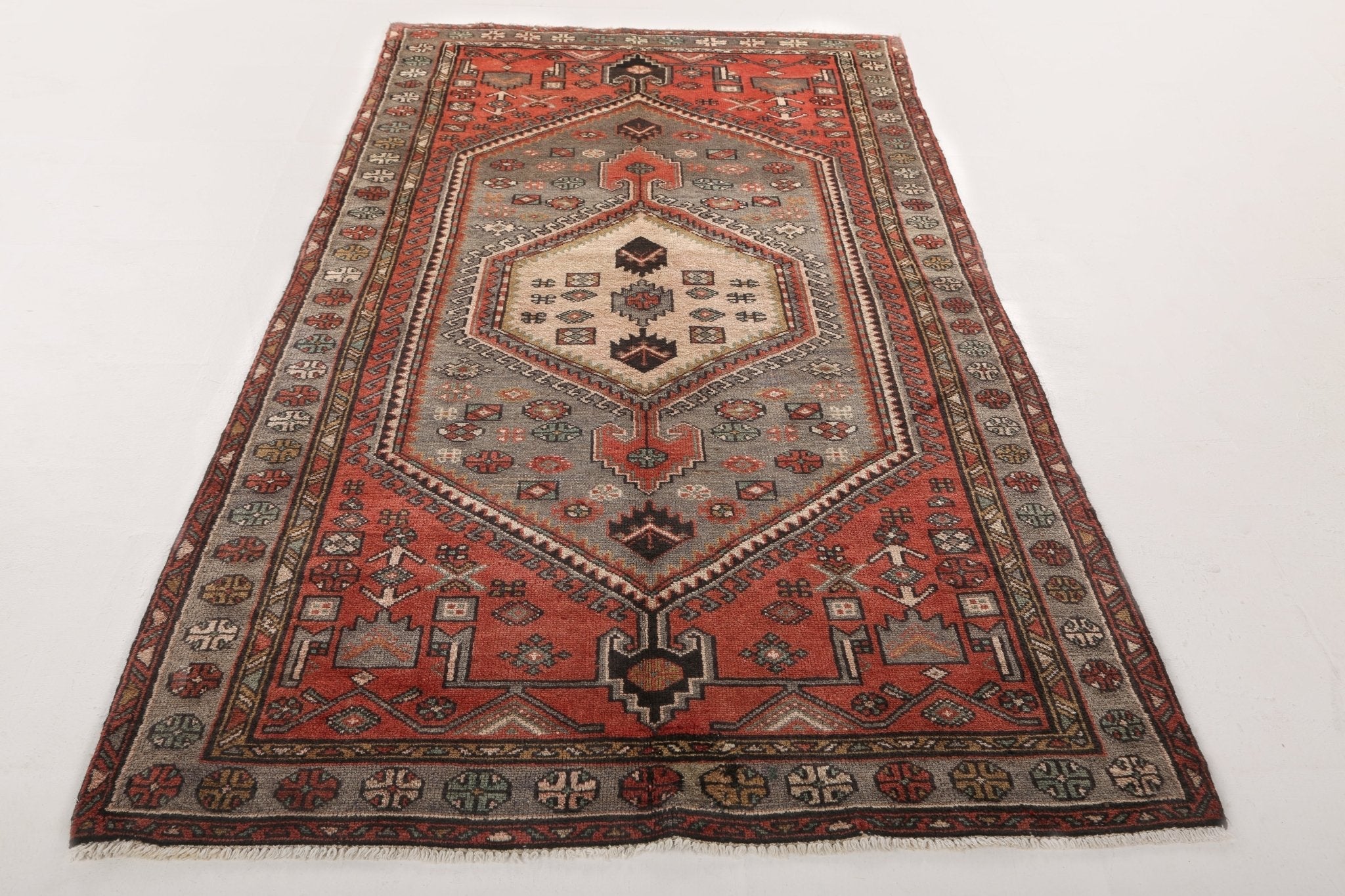 Persian-style area rug featuring central medallion, rust-red field, gray accents, cream details.