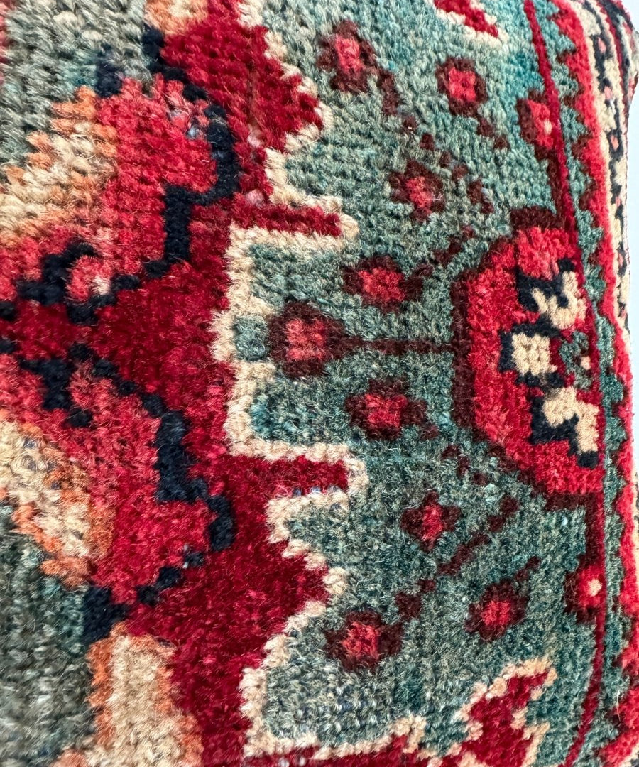 Decorative square pillow close-up with red and teal geometric embroidery on cream