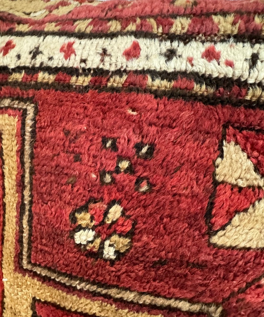 Close-up of red throw pillow face with cream floral and star-like embroidery motifs.