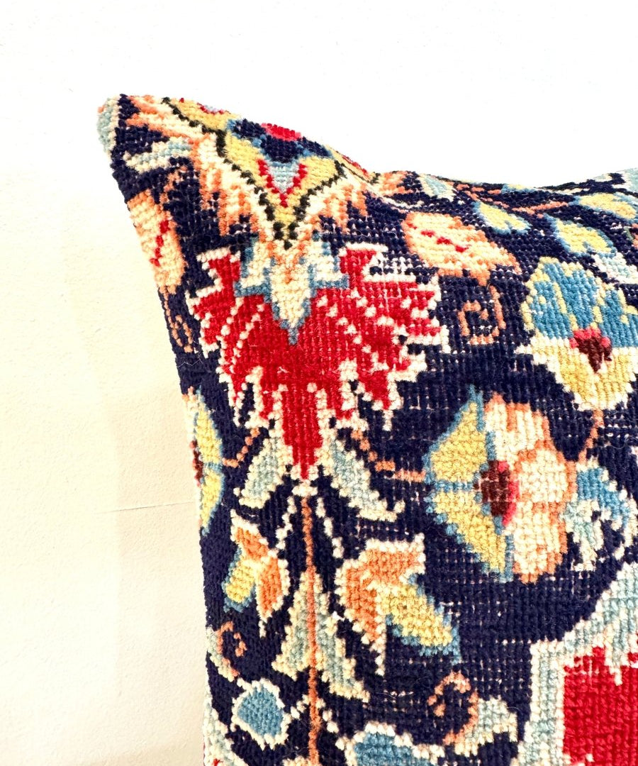 Square decorative pillow corner, red and navy embroidered floral geometric pattern.