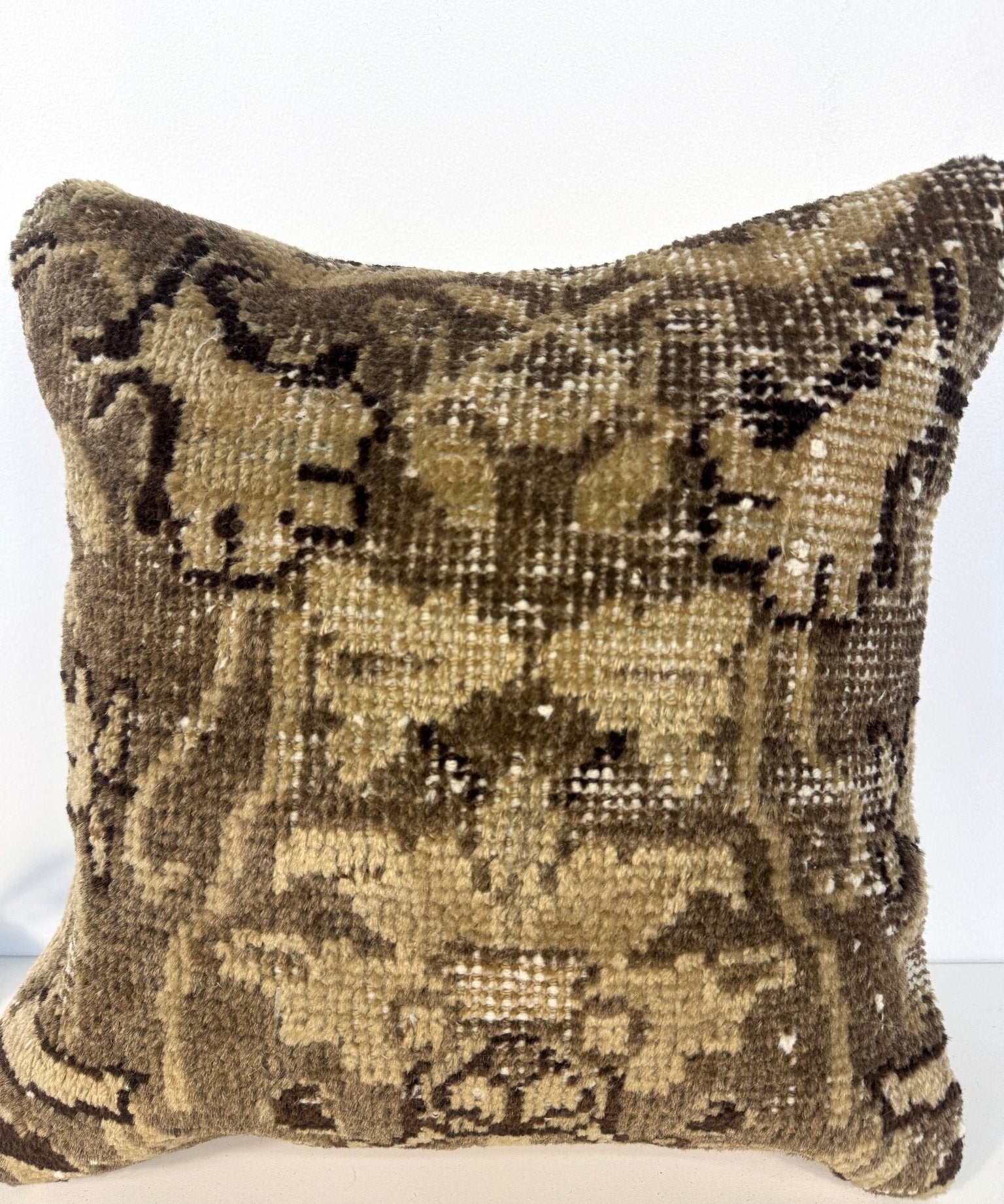 Square decorative pillow with olive and dark abstract geometric pattern; visible side seam and piping