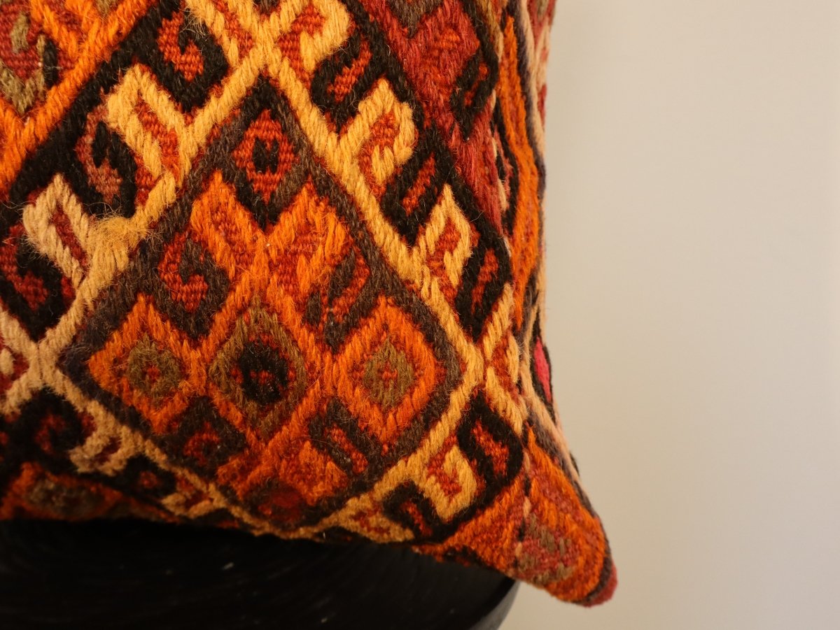 Corner of geometric embroidered pillow cover with orange, black, cream, and red pattern, 16 in