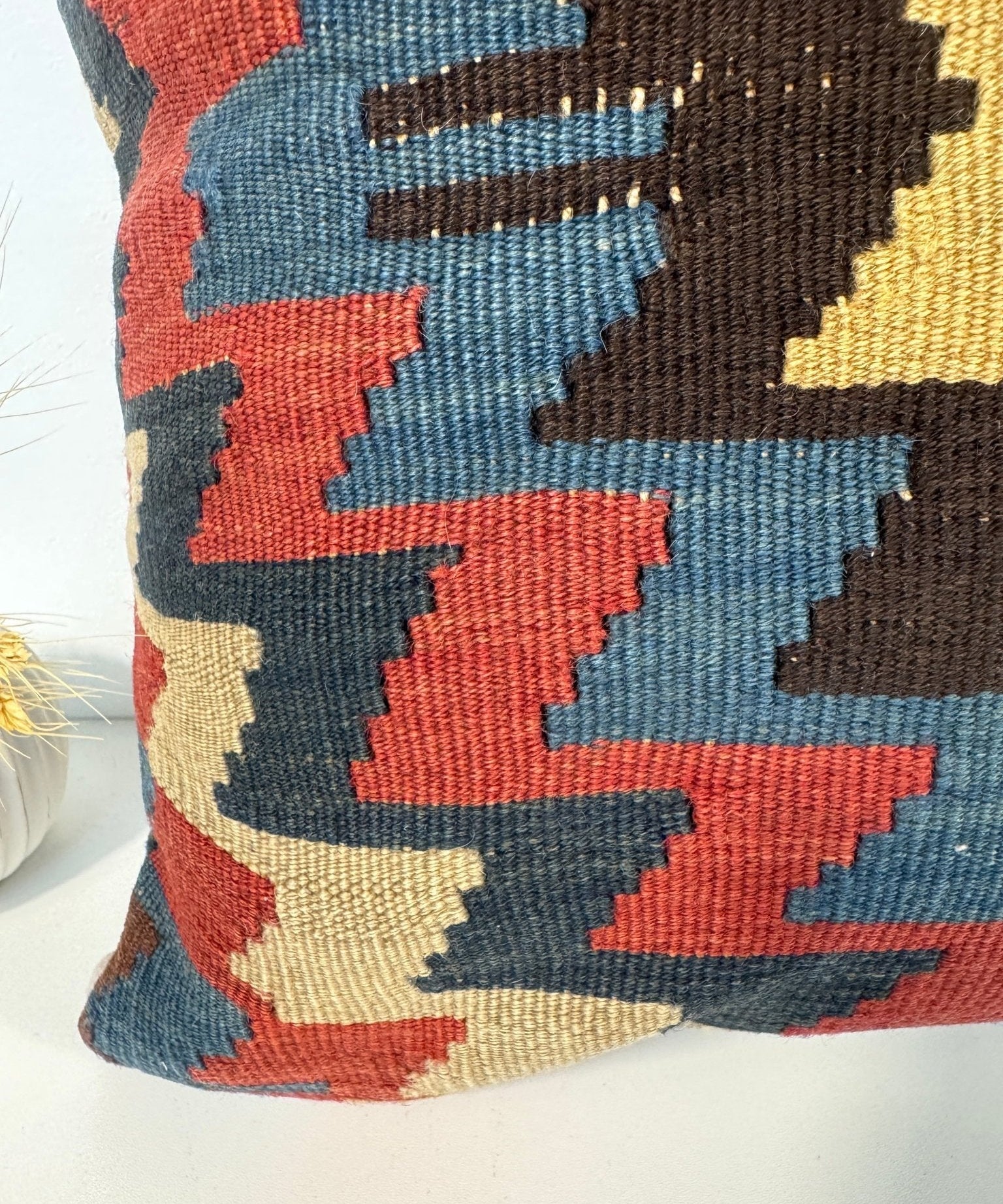 Decorative pillow close-up showing red, blue, beige, and dark diamond shapes.