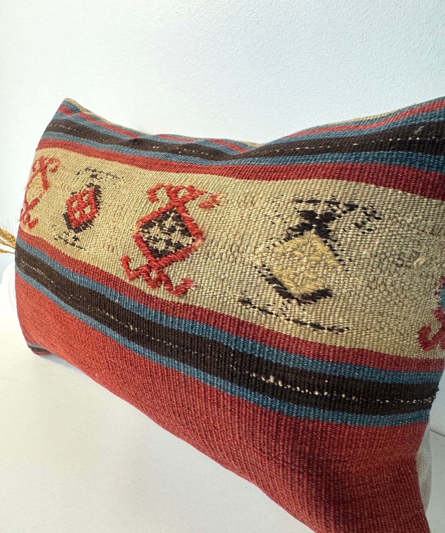Woven lumbar pillow side view with beige base, red motifs, and dark striped border