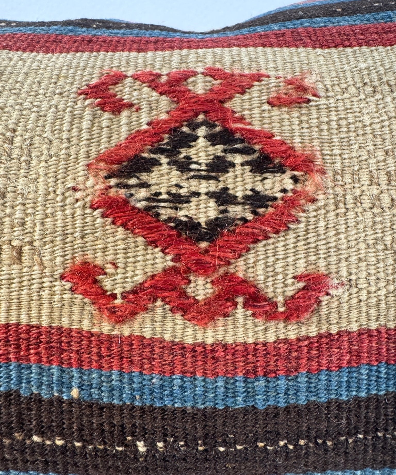 Close-up of embroidered diamond motif on beige woven pillow fabric with striped bands