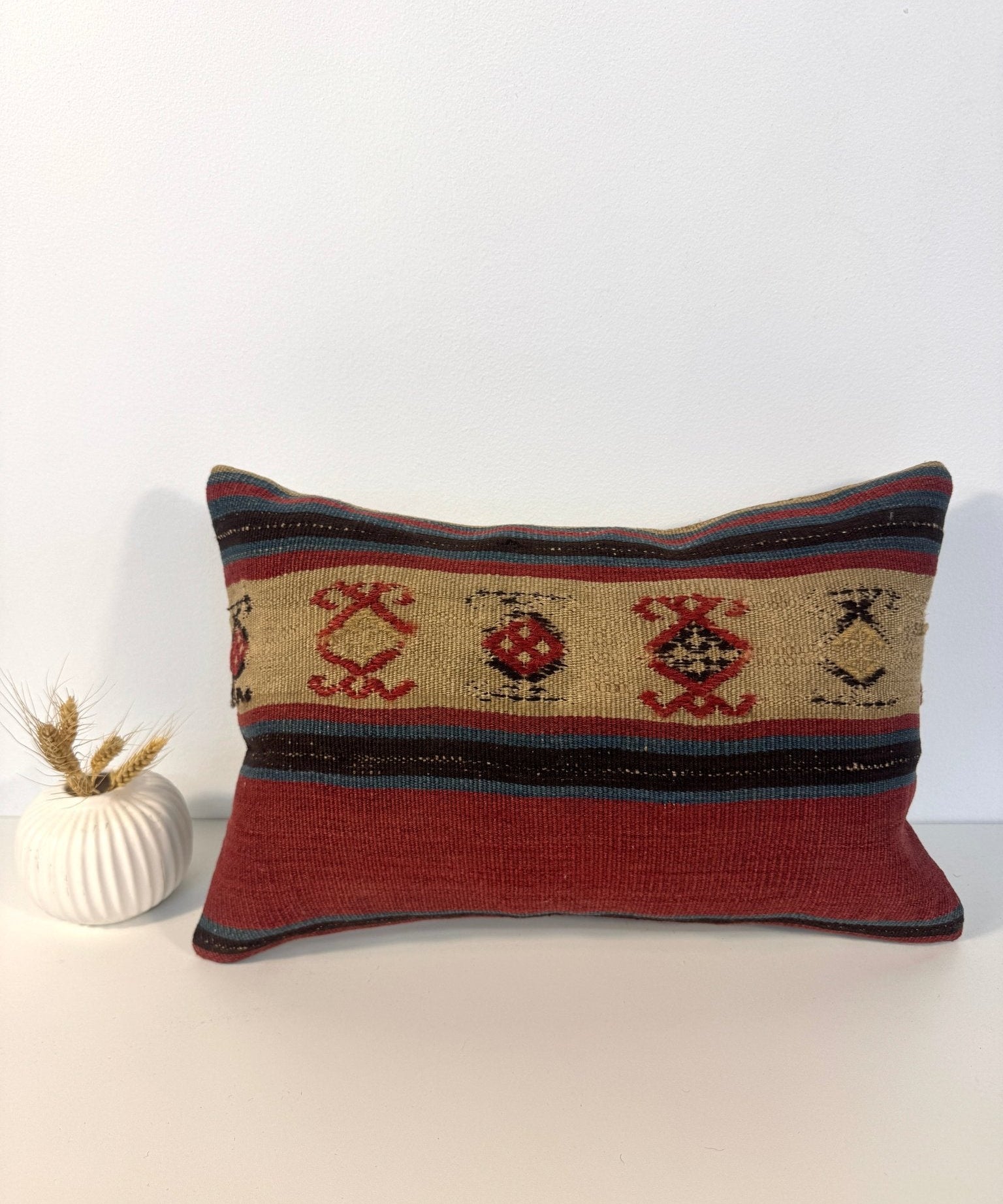 Woven lumbar pillow with beige base, red motifs, and multicolor striped border