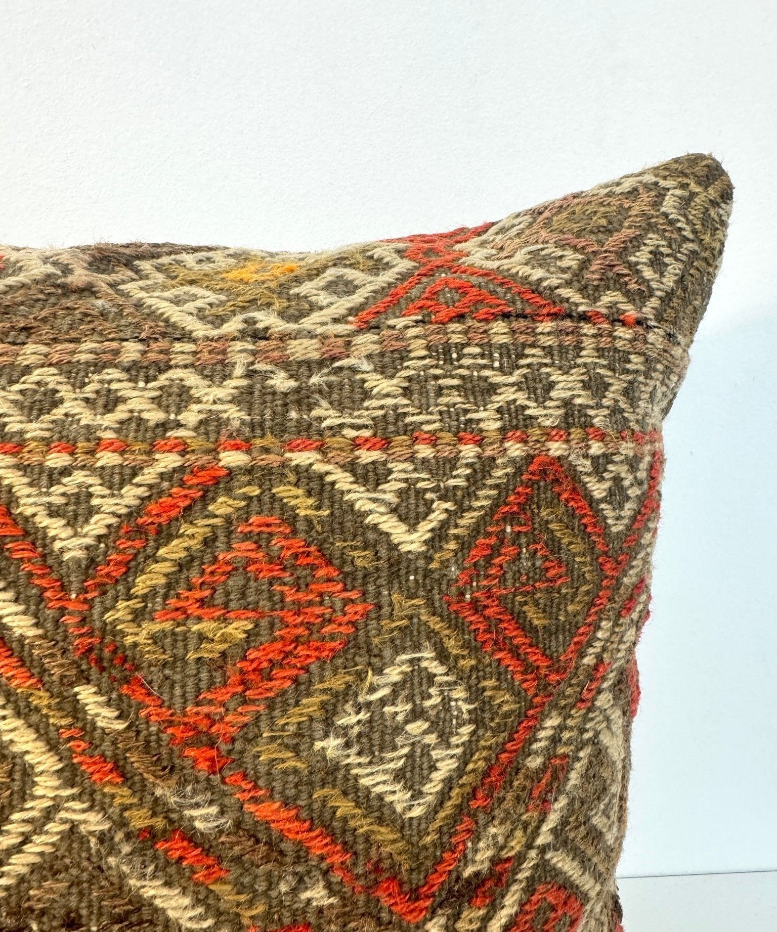Woven throw pillow cover in dark brown with red geometric stitching, corner view