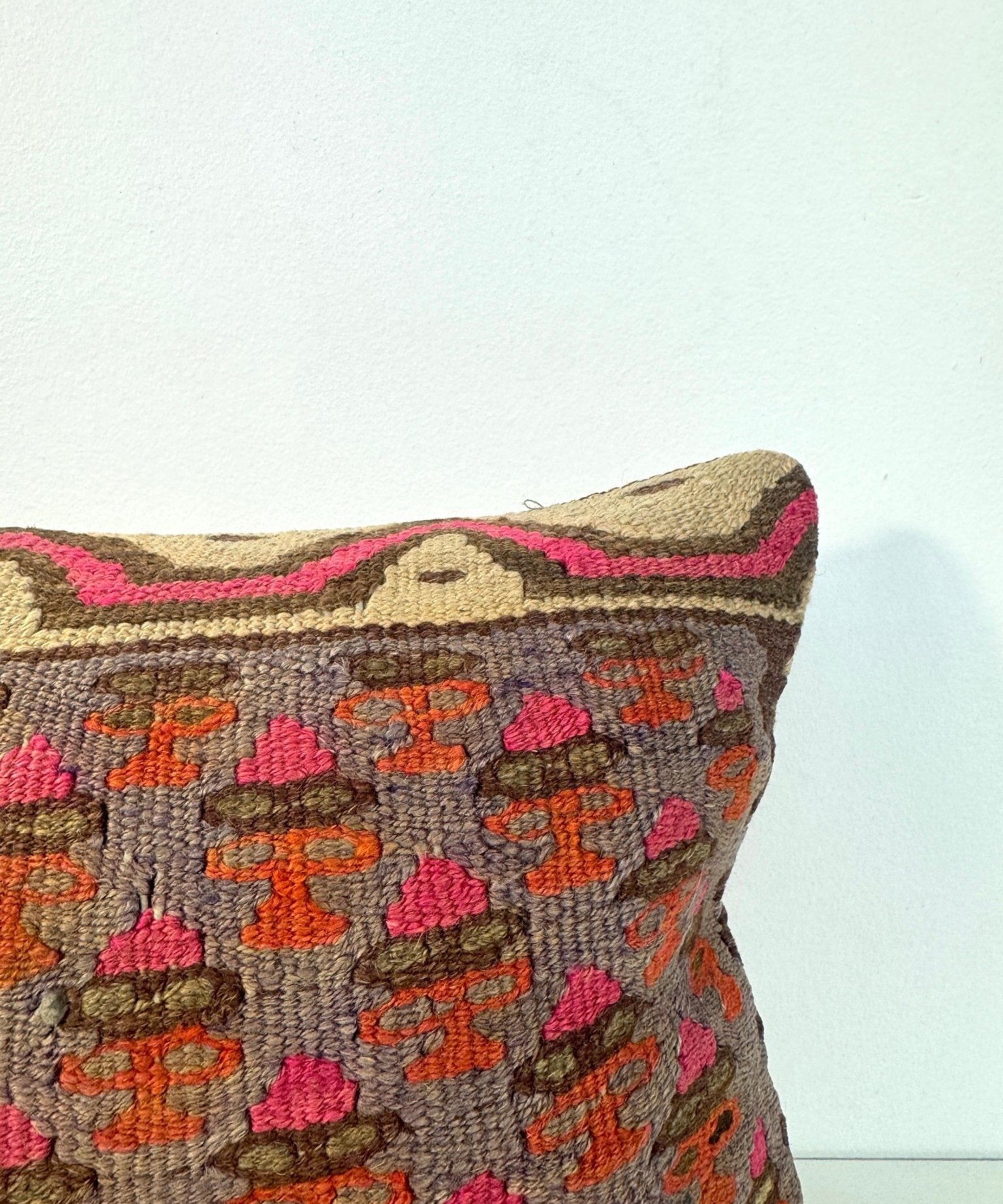 Embroidered throw pillow corner, gray with orange and pink motif pattern, braided trim