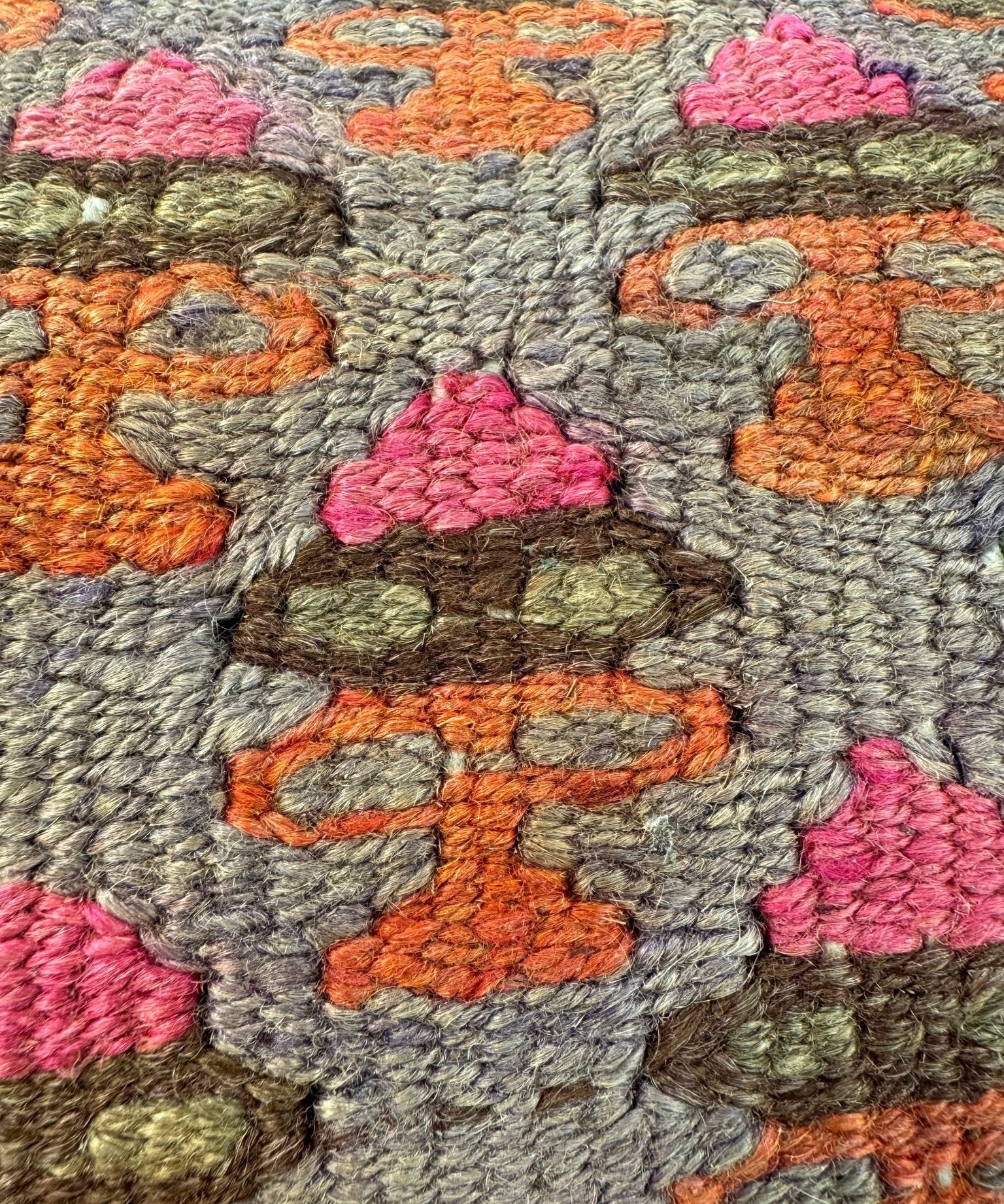 Textured embroidered pillow fabric with gray base and orange, pink, and green motifs