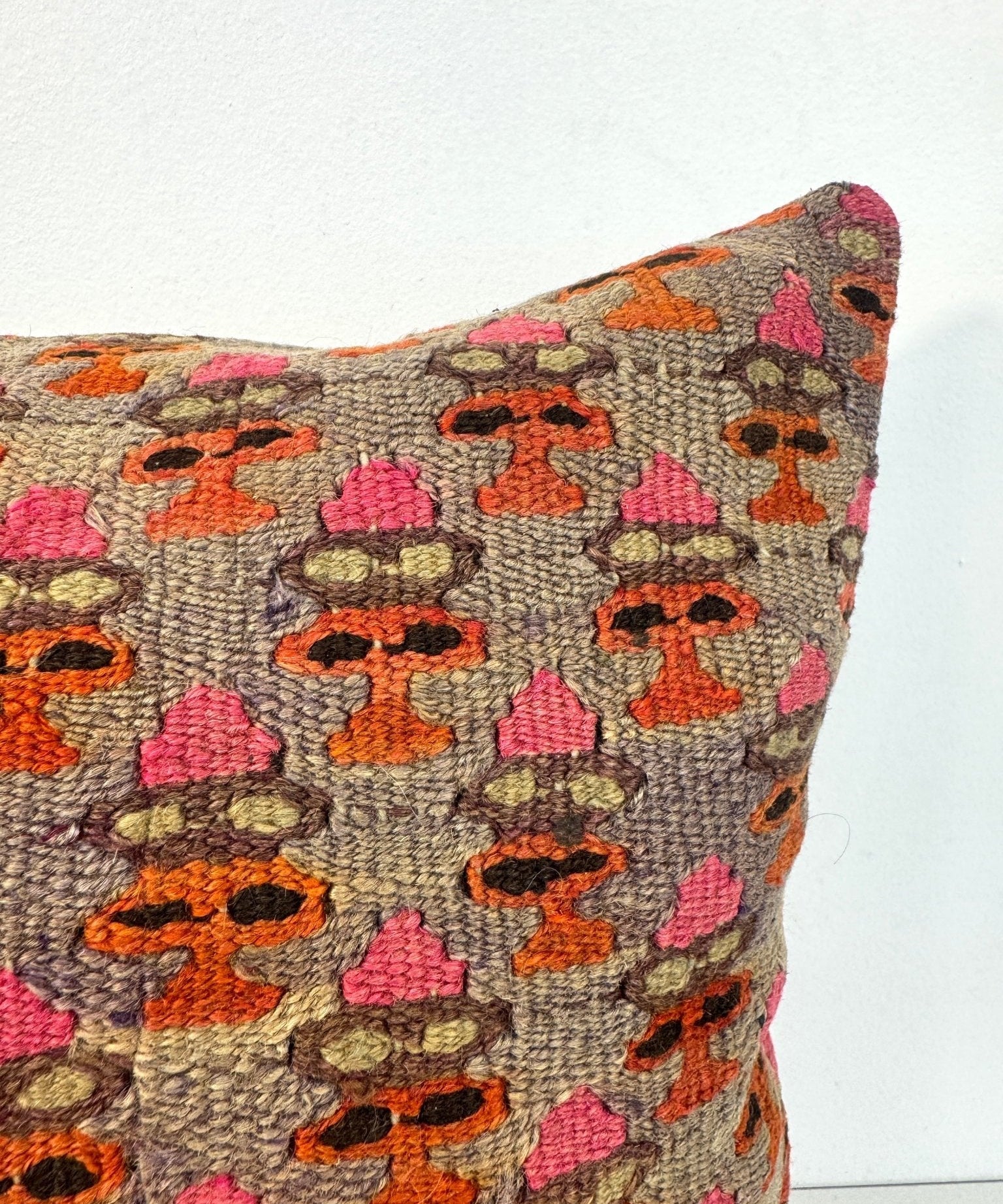 16x16 pillow close-up: multicolor geometric embroidery on textured gray fabric