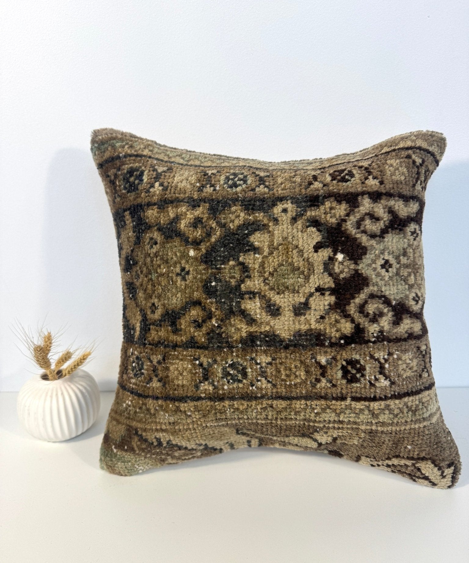 Square decorative pillow with olive-brown patterned woven front and dark stitched border
