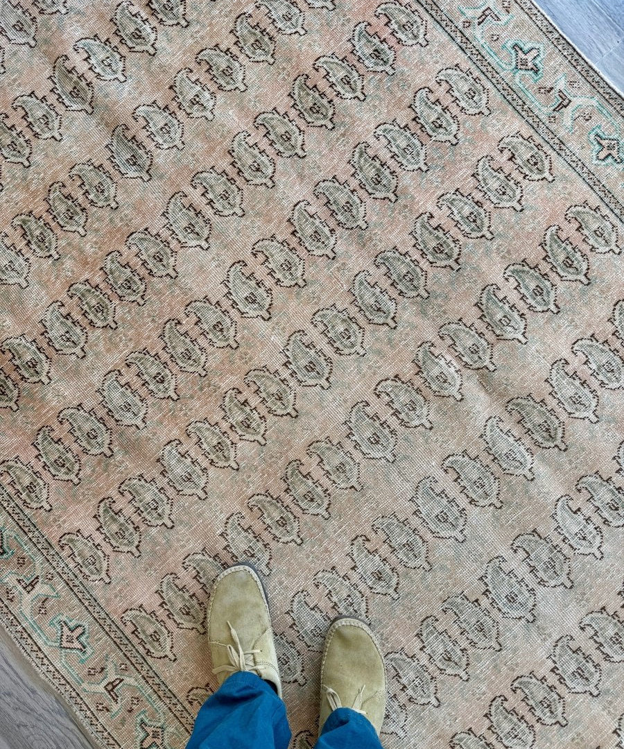 Beige Tabriz-style paisley rug with repeating medallion pattern and dark teal border
