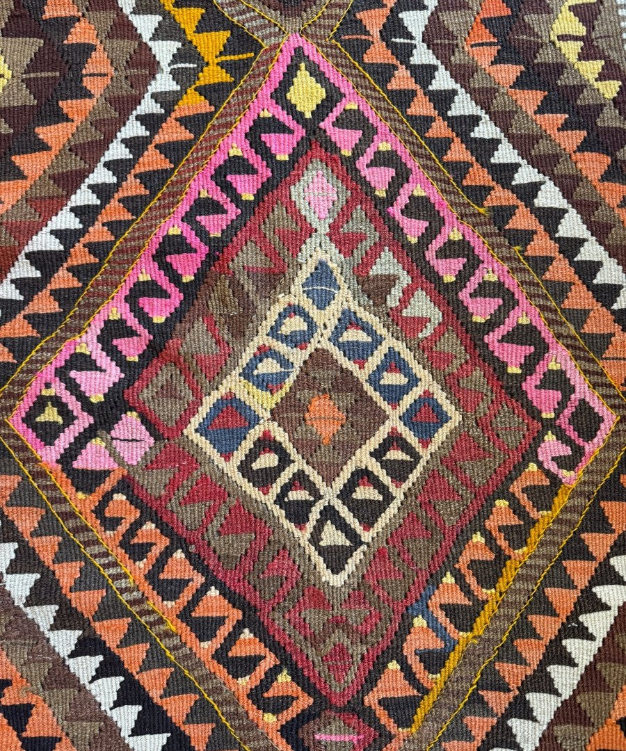 Close-up kilim rug section with diamond medallion, zigzag borders, and pink accents.