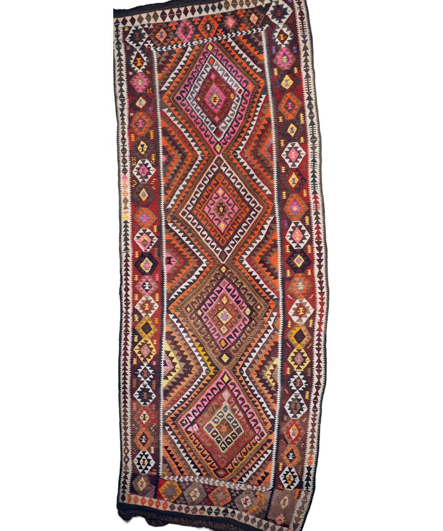 Kilim rug with dark border, central medallion, multicolor geometric motifs, and tassels.