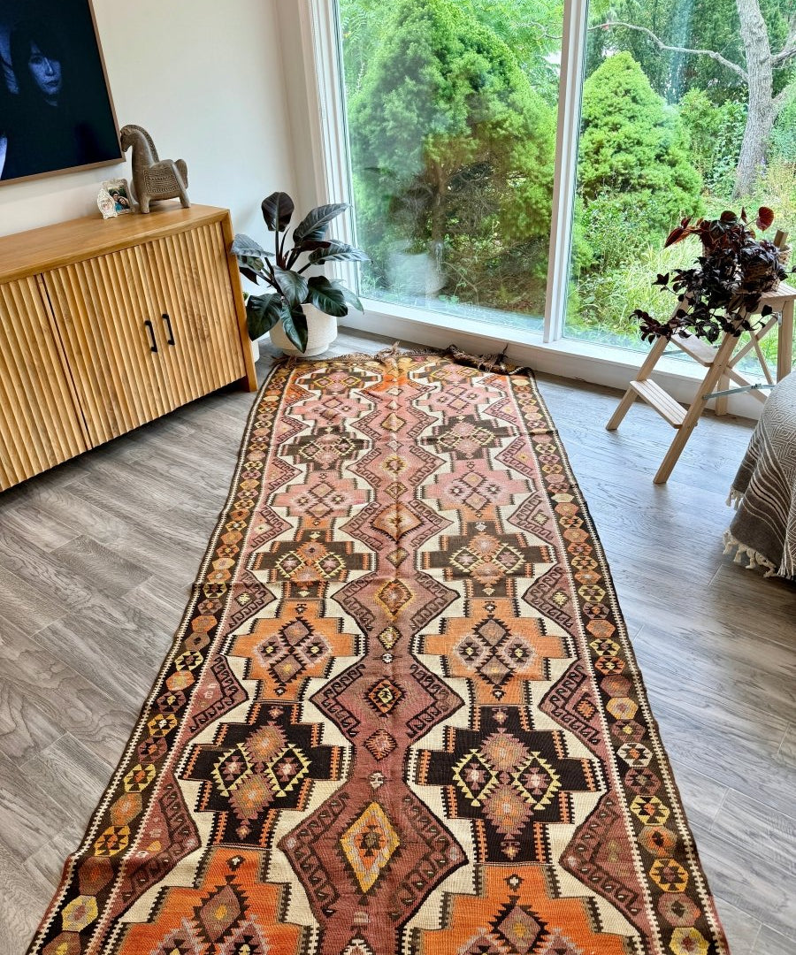 Kilim runner rug featuring orange, pink, black, and cream geometric motifs.