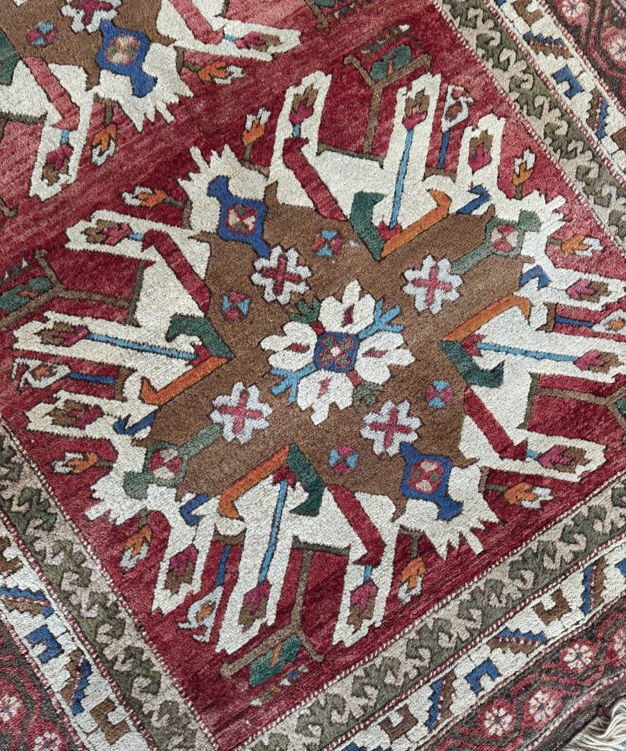 Turkish Kars rug corner detail with maroon field, ivory border, and blue, tan, and rust geometric shapes.