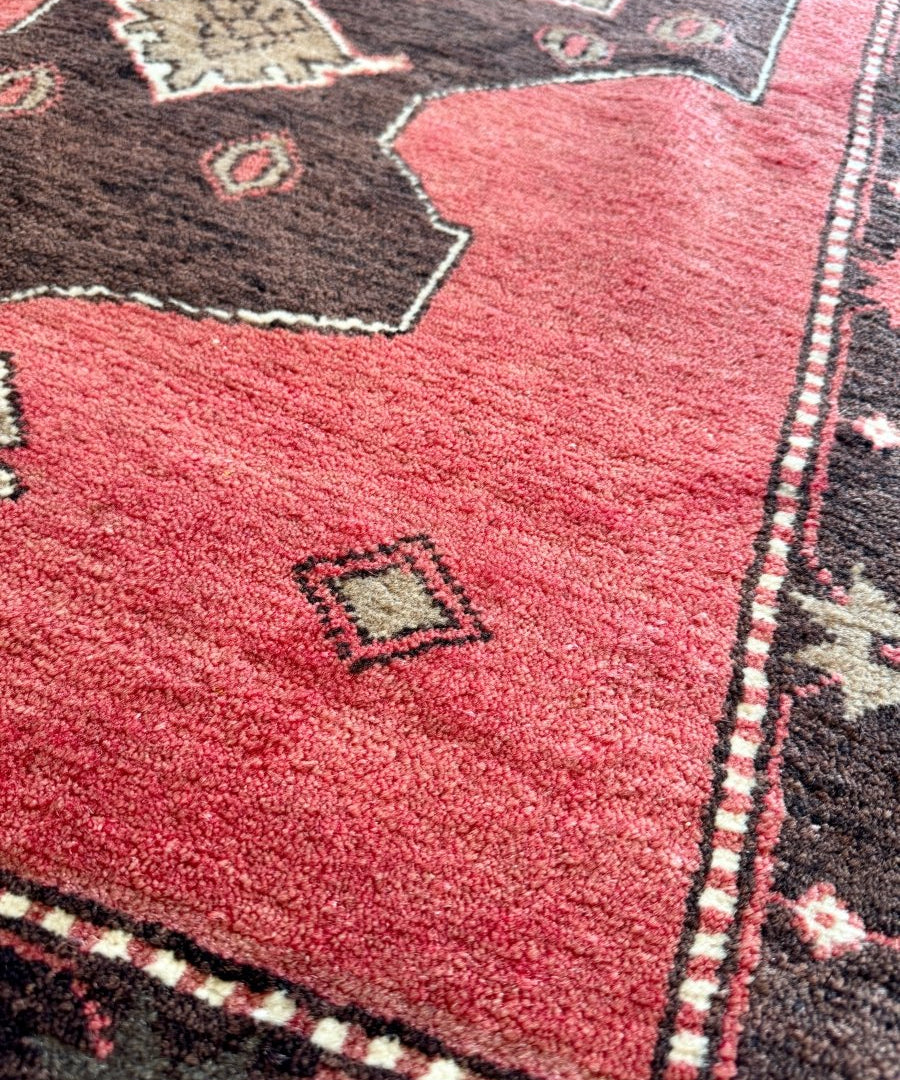Red rug close-up with black corner motifs, diamond pattern, and fringed border