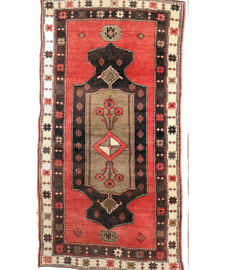 Rectangular red Turkish rug with central black medallion, cream border, and small motifs
