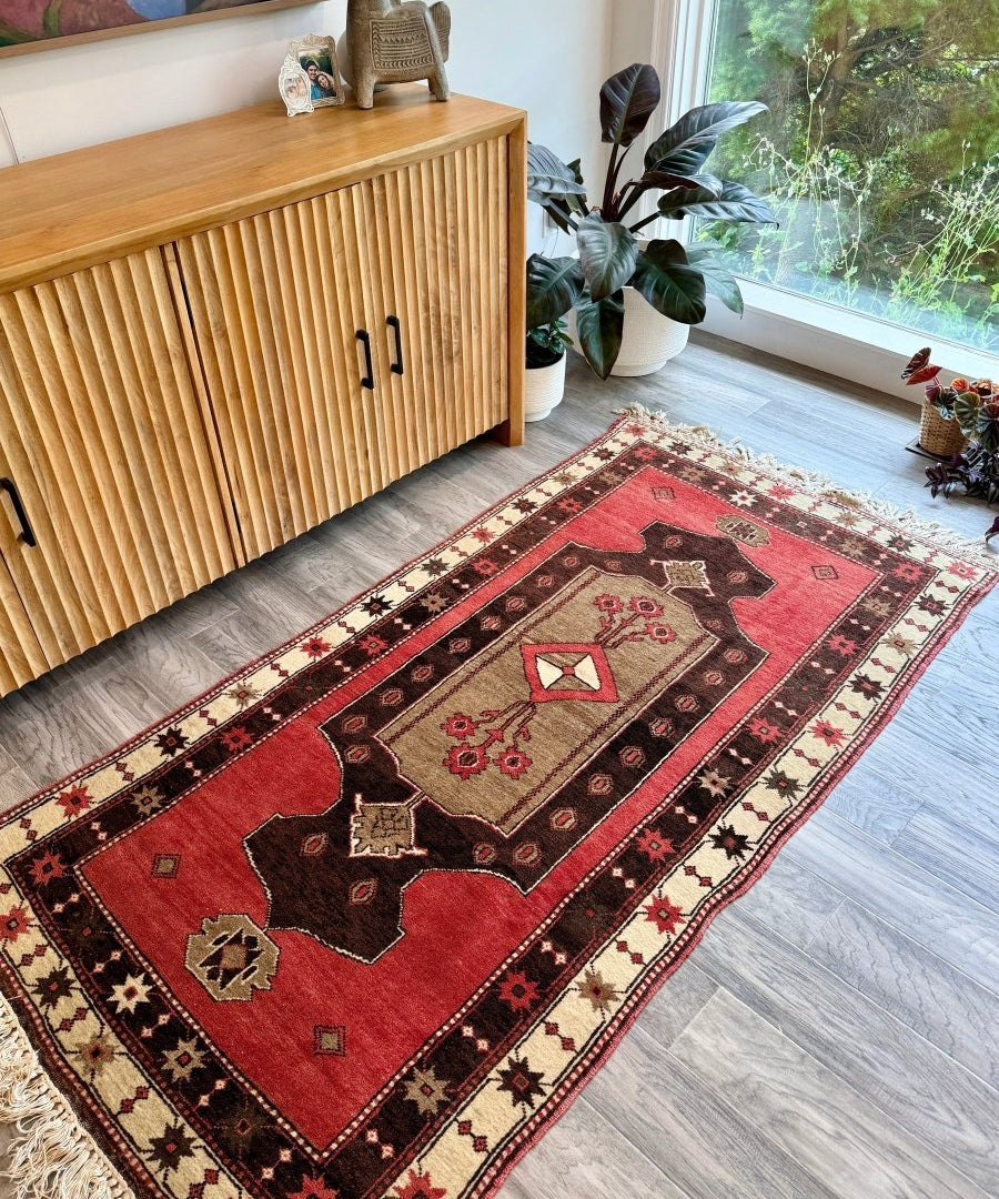 Red Turkish rug with central black medallion, diamond accents, and cream border