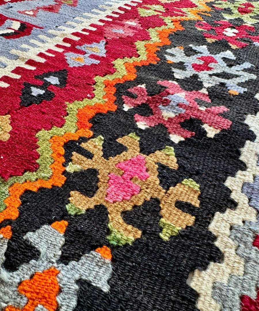 Close-up of Turkish kilim rug weaving with colorful geometric shapes on dark background.