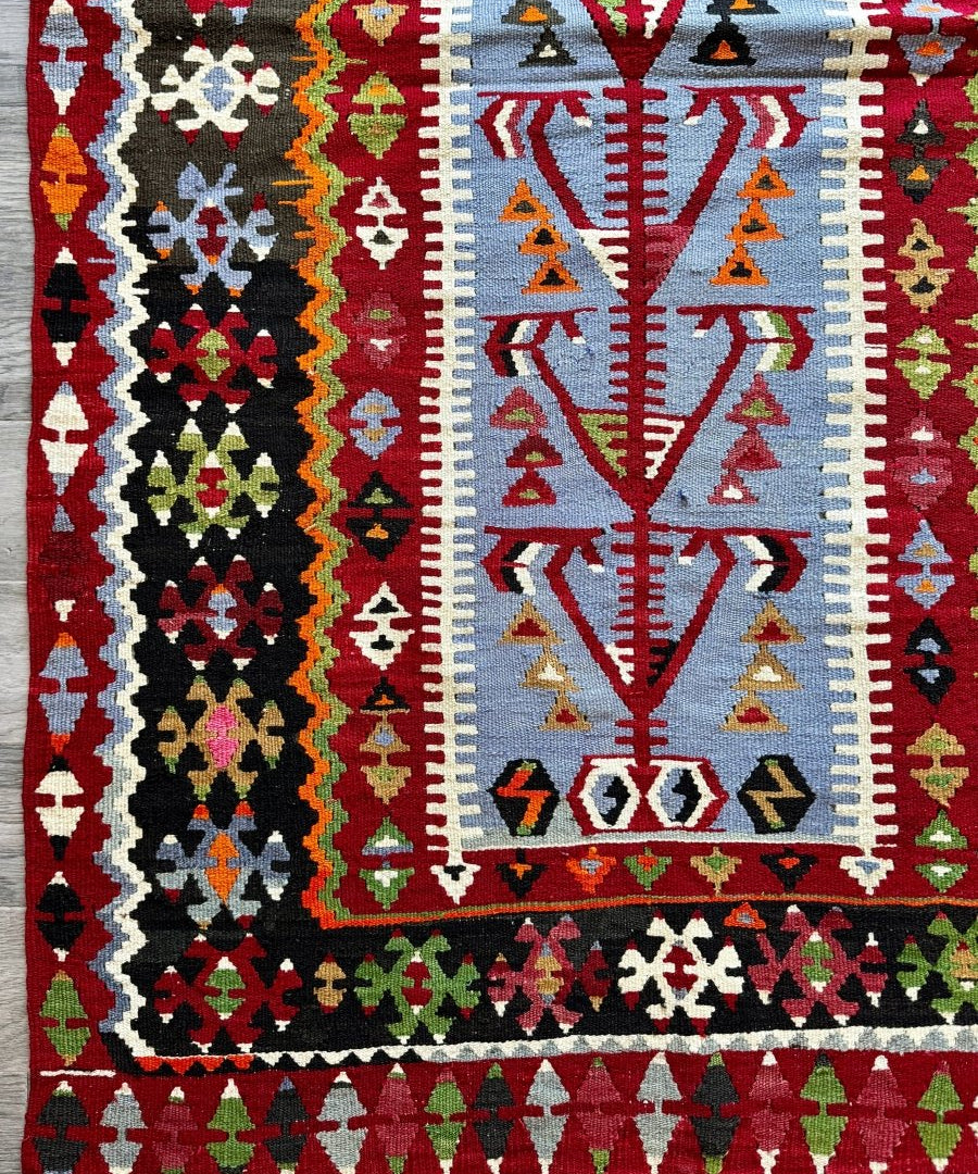 Colorful Turkish kilim rug with red border, geometric motifs, and black center panels.