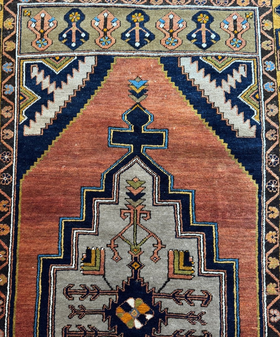 Turkish patterned area rug with rust center, navy corner bands, and teal framed cross motif.